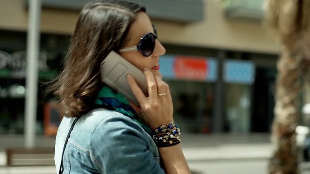 Young woman walking in the city and talking on cellphone, steadycam shot

