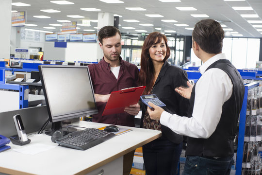 Sales assistant advising couple on cost in electronics store