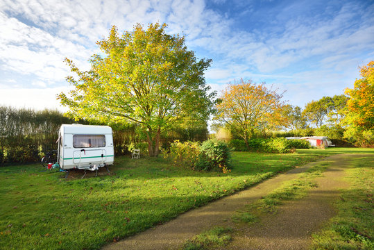 Caravan trailer on a green lawn under the trees, on a sunny spri
