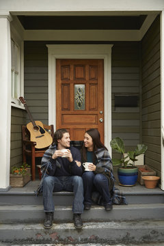 Young Couple Sitting On Porch Step Chatting