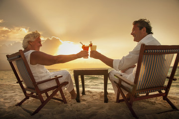 Senior couple toasting drinks on beach, Maldives
