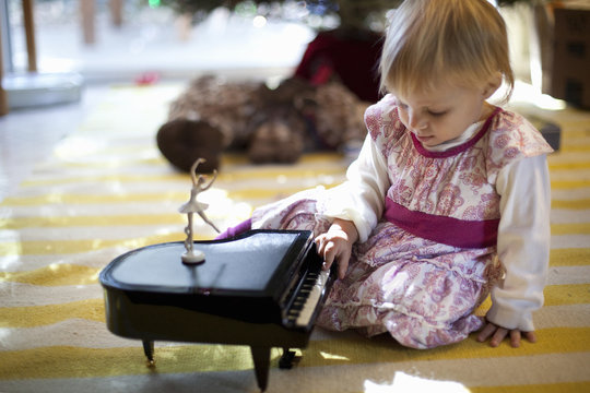 Female toddler sitting on living room floor playing with toy piano music box at Xmas