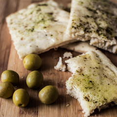 Three tasty slices of italian focaccia (one half eaten) with herbs and some olives on the side - square.