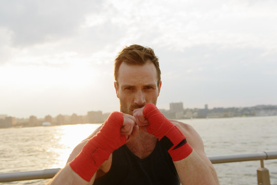 Portrait of young male boxer exercising on riverside