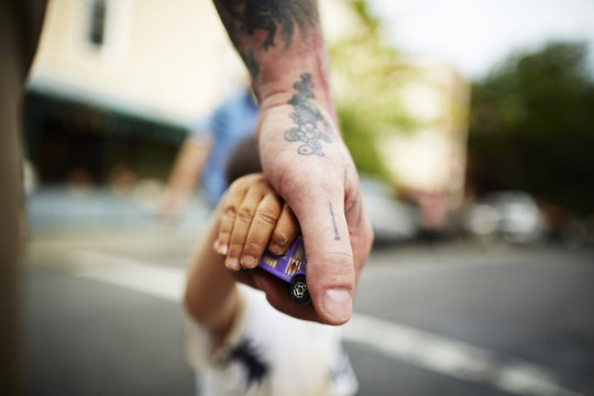 Close up of man holding boy's hand and toy crossing road