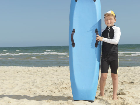 Portrait of boy nipper (child surf life savers) next to surfboard, Altona, Melbourne, Australia