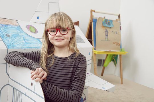 Portrait of young girl standing next to cardboard spaceship