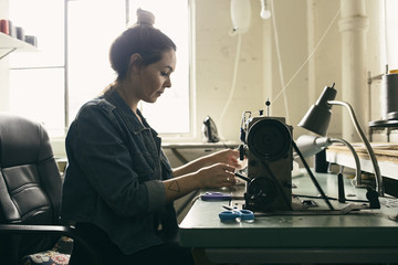 Young female seamstress using sewing machine in fashion studio