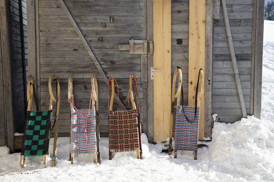 Row of four sledges leaning against log cabin