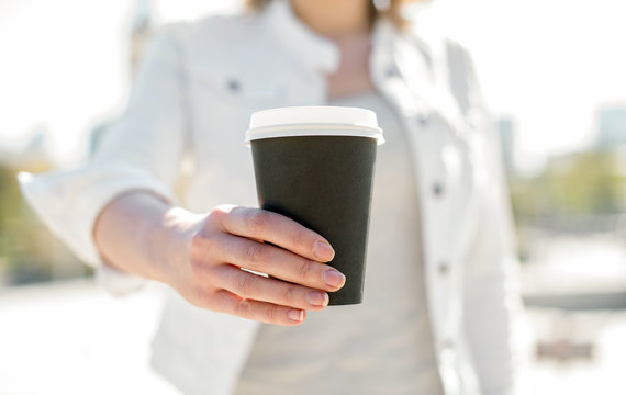 Woman's hands offering coffee cup outdoors.