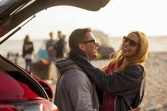 Couple Relaxing Behind Vehicle On Beach