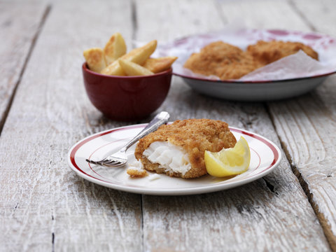 Breaded chunky cod with bowl of french fries on wooden table