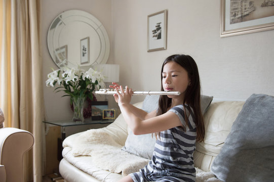 Girl practicing the flute on sofa