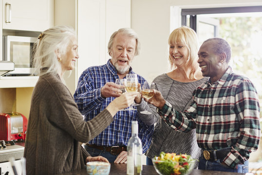 Senior friends toasting wine glasses in the kitchen - Powered by Adobe