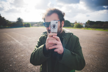 Portrait of mid adult man pointing vintage movie camera on waste ground