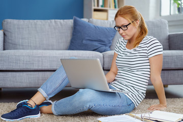 junge frau sitzt auf dem boden im wohnzimmer mit laptop und unterlagen