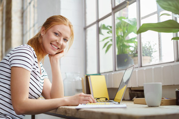 frau sitzt mit laptop an einem tisch am fenster