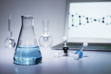 Chemistry research. Erlenmeyer flask containing colored liquid, a ball-and-stick molecular model and laptop computer
