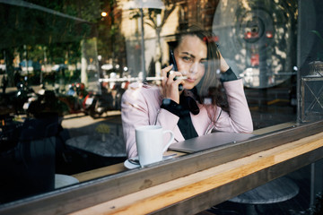 young modern business woman uses a smartphone for business call while having breakfast in the cafe.beautiful girl talking on the phone while sitting near the panoramic window in the cozy coffeehouse.