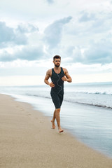 Fototapeta na wymiar Sports. Handsome Fit Athletic Man Running On Beach. Sporty Runner Jogging Near Sea During Outdoor Workout. Healthy Active Jogger Exercising And Training For Marathon. Fitness Concept