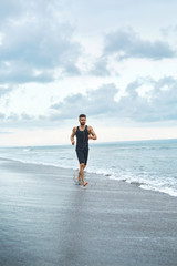 Fototapeta na wymiar Sports. Handsome Fit Athletic Man Running On Beach. Sporty Runner Jogging Near Sea During Outdoor Workout. Healthy Active Jogger Exercising And Training For Marathon. Fitness Concept