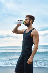 Man Drinking Water After Running Workout At Beach. Portrait Of Thirsty Healthy Athletic Male With Fit Body Drinking Refreshing Drink, Resting After Running Or Training Outdoor. Sports, Fitness Concept
