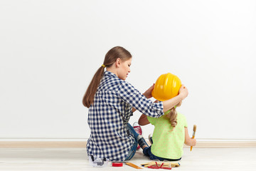 Young woman putting on her daughter protective helmet sitting on the floor in empty room.  Concept of flat renovation and wall coloring.   - 110964646