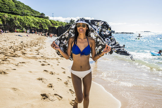 Young woman wearing bikini holding scarf over her head on  Waimea Beach, Oahu, Hawaii, USA