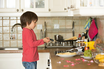 Sweet preschool child, helping his mom in the kitchen, making pa