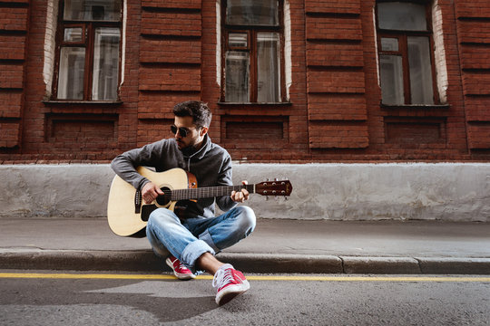 Handsome man is playing on guitar sitting on the road