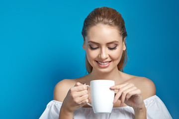 Beautiful young woman holding a white cup of drink and smiling on blue background