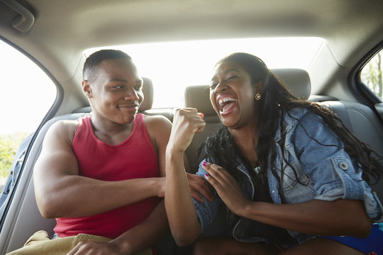 Young couple in car laughing, woman flexing muscles