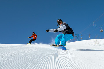 Group of two snowboarders riding over the slope prepared by snowcat. Sheregesh resort, Siberia, Russia