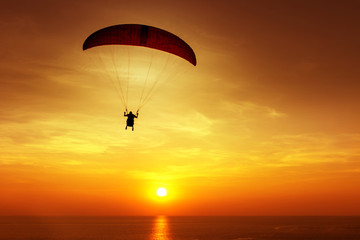 Silhouette of skydiver flies on background of sunset sky and sea
