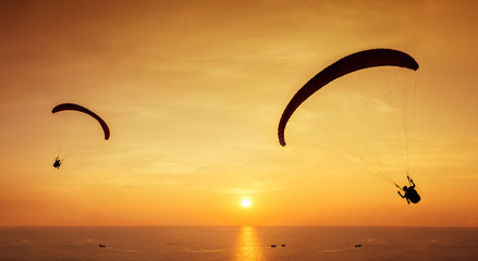 Two silhouettes of skydivers are flies on background of sunset sky and sea