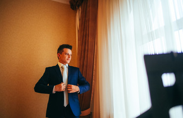 happy gorgeous handsome groom getting ready dressed in the morning on background of a room