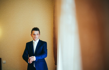 happy gorgeous handsome groom getting ready dressed in the morning on background of a room
