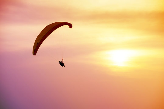Silhouette of sky diver flies on background of sunset sky