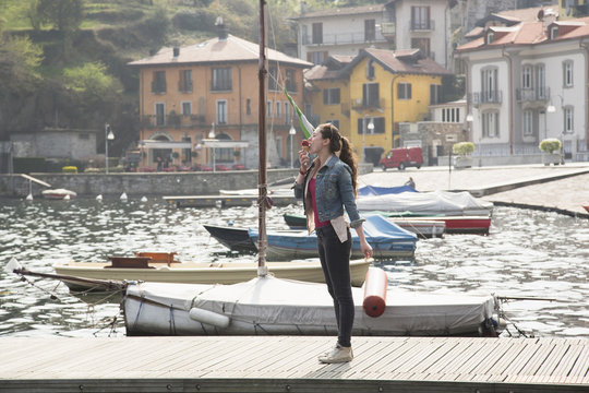 Young woman standing on pier eating ice cream cone at lake Mergozzo, Verbania, Piemonte, Italy