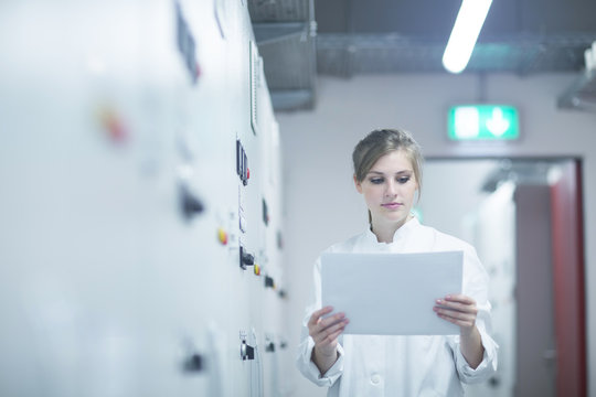 Young female scientist reading paperwork in technical room