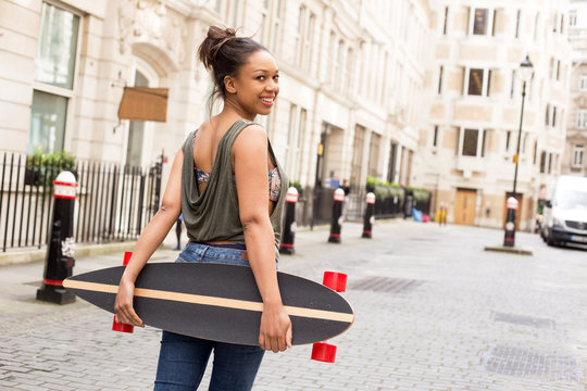 a young woman looking back holding a skateboard