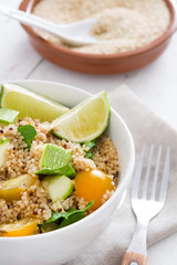 Quinoa salad in bowl, tomatoes and spinach on white wooden table
