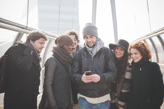 Six young adult friends on footbridge reading smartphone text