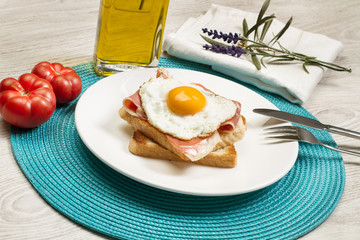 Plato con huevo frito con jamón y pan sobre plato blanco. Vista de frente