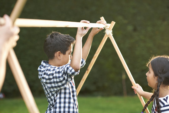 Brother and sister putting up homemade tent frame in garden