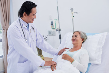 Vietnamese doctor reassuring senior female patient before surgery