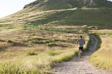 Rear view of young male runner running up hillside track
