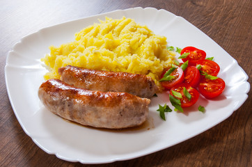 fried meat sausages with mashed potatoes and vegetables salad in a plate on wooden table