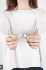 woman with white jersey breaking a cigarette tobacco with her two hands over white background
