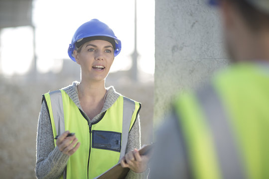 Female surveyor with clipboard talking to builder on construction site